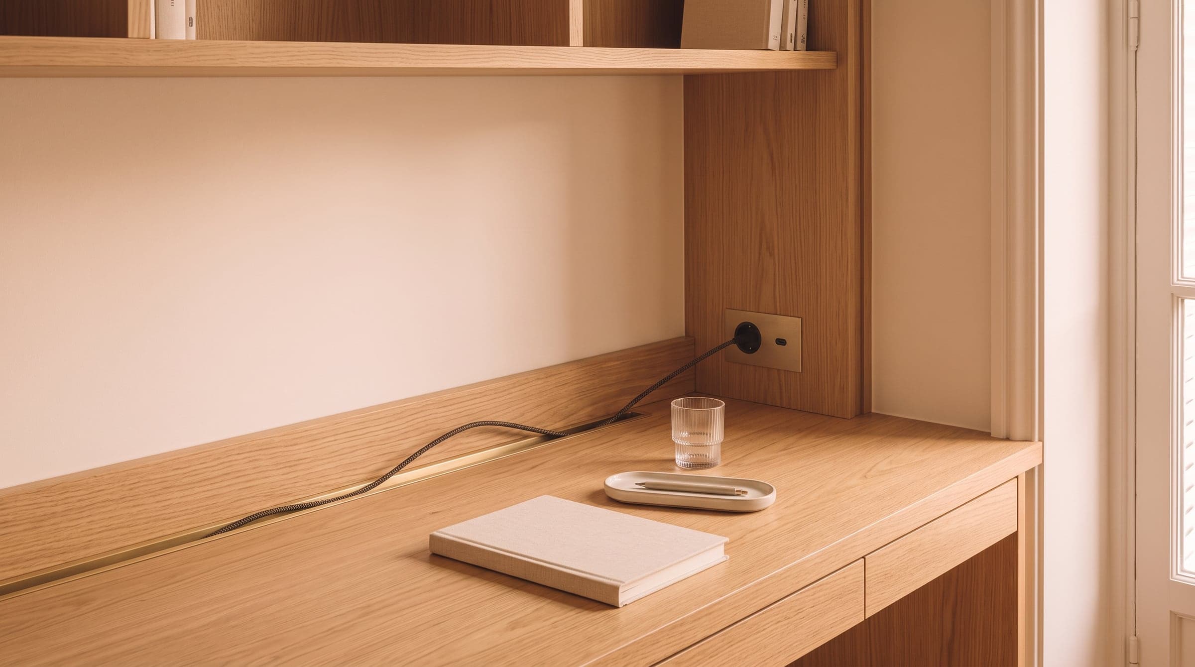 Close view of a built-in desk with a cable channel along the back edge and a socket set into the side panel