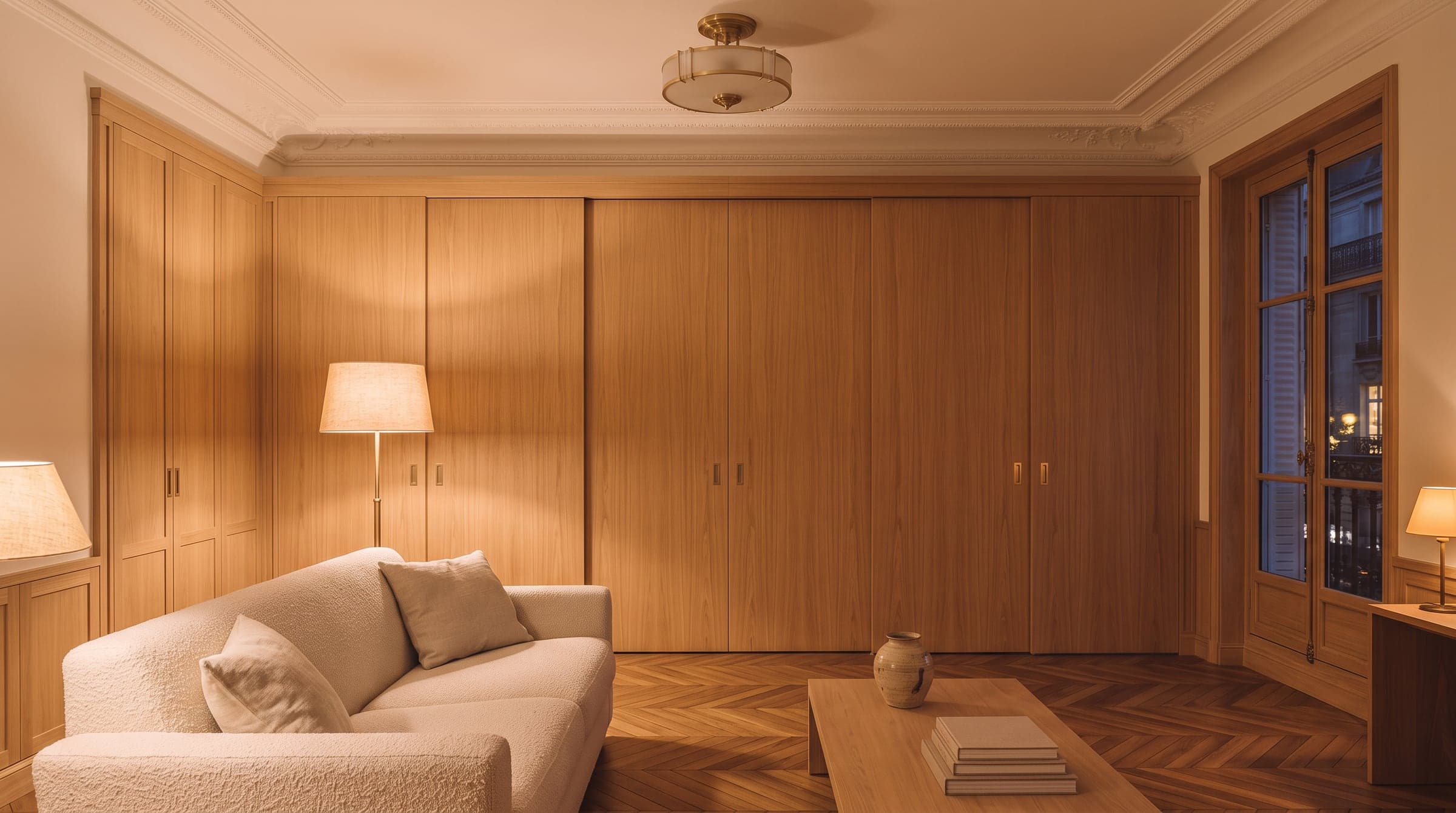 A built-in desk closed behind matching oak sliding doors in the evening, the living room lit for the end of the day