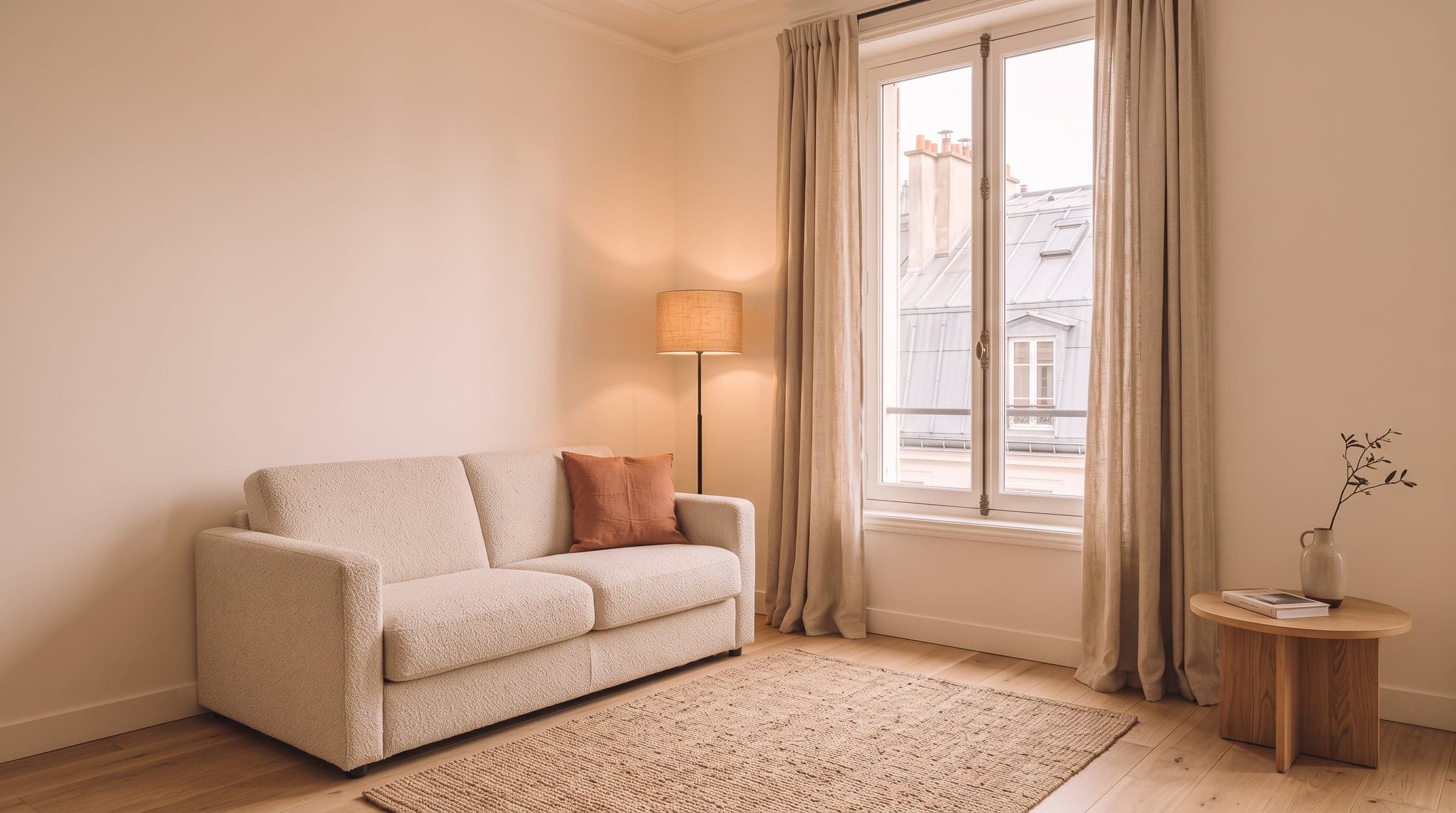 Simple Paris living room corner with a bouclé sofa, a terracotta cushion and a jute rug, the architecture untouched