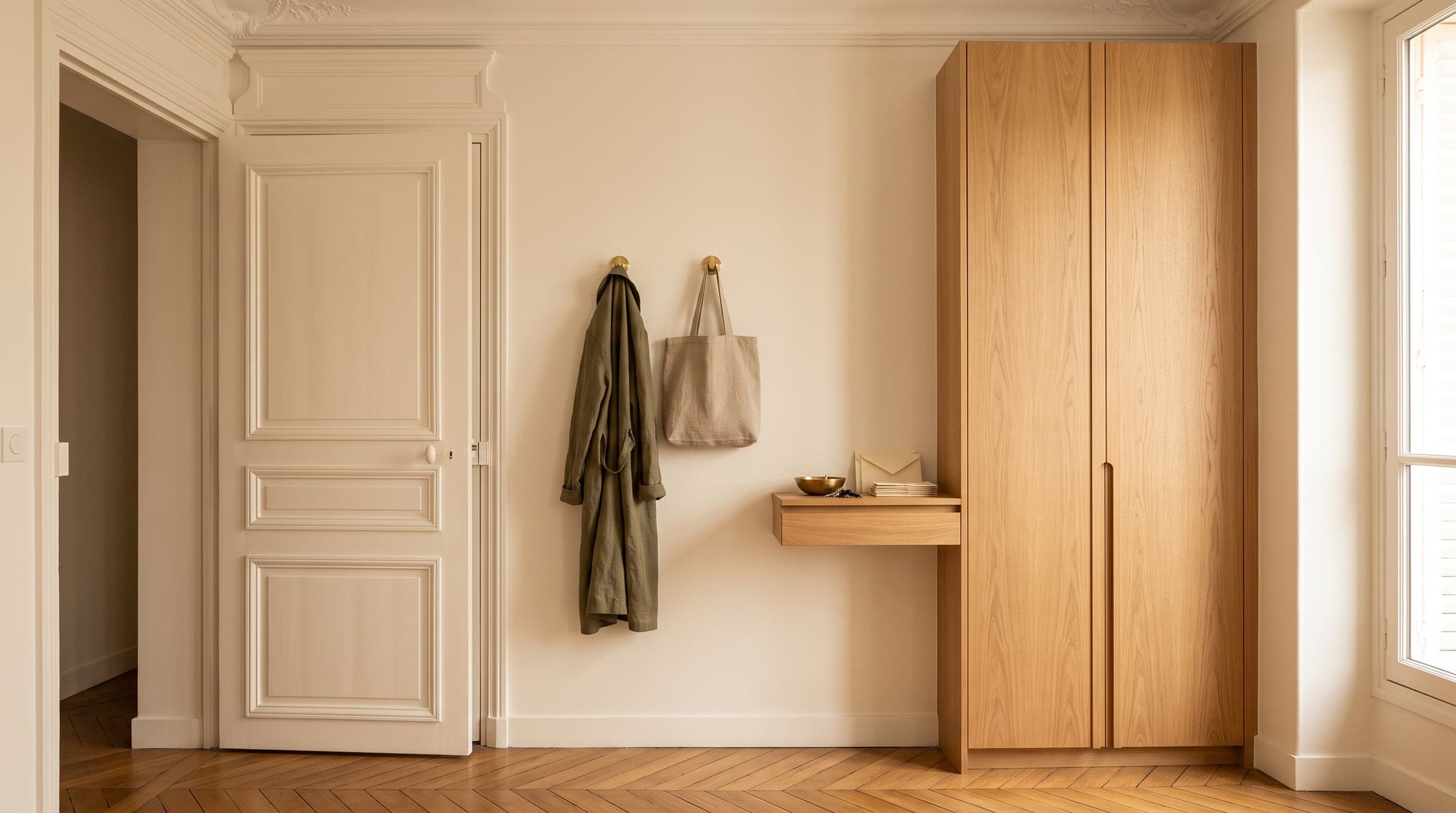 Meuble d'entrée fermé à hauteur de porte avec deux patères apparentes pour le manteau du quotidien