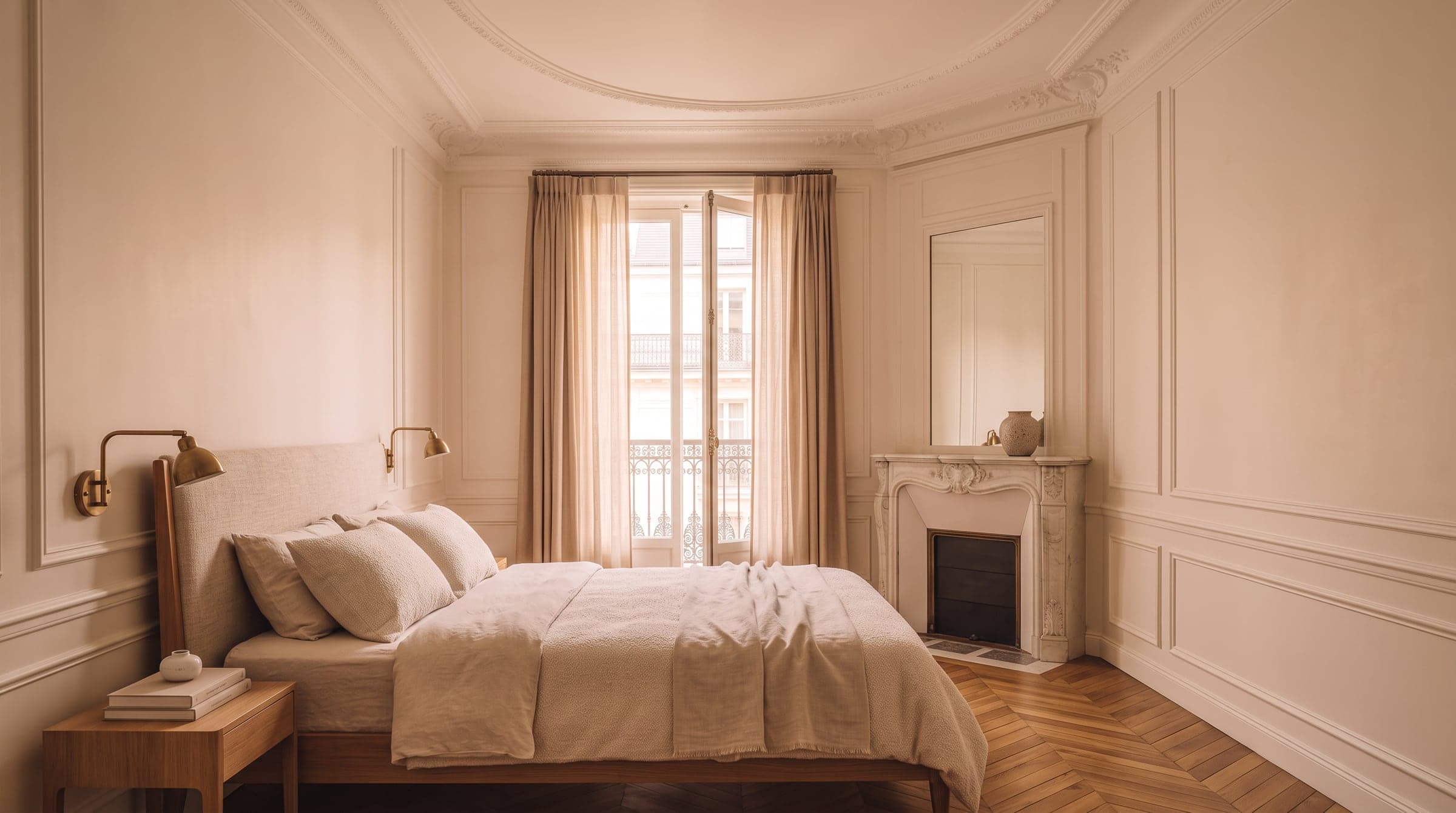 Calm bedroom with pale plaster walls, oak flooring and a tall French window open to evening light