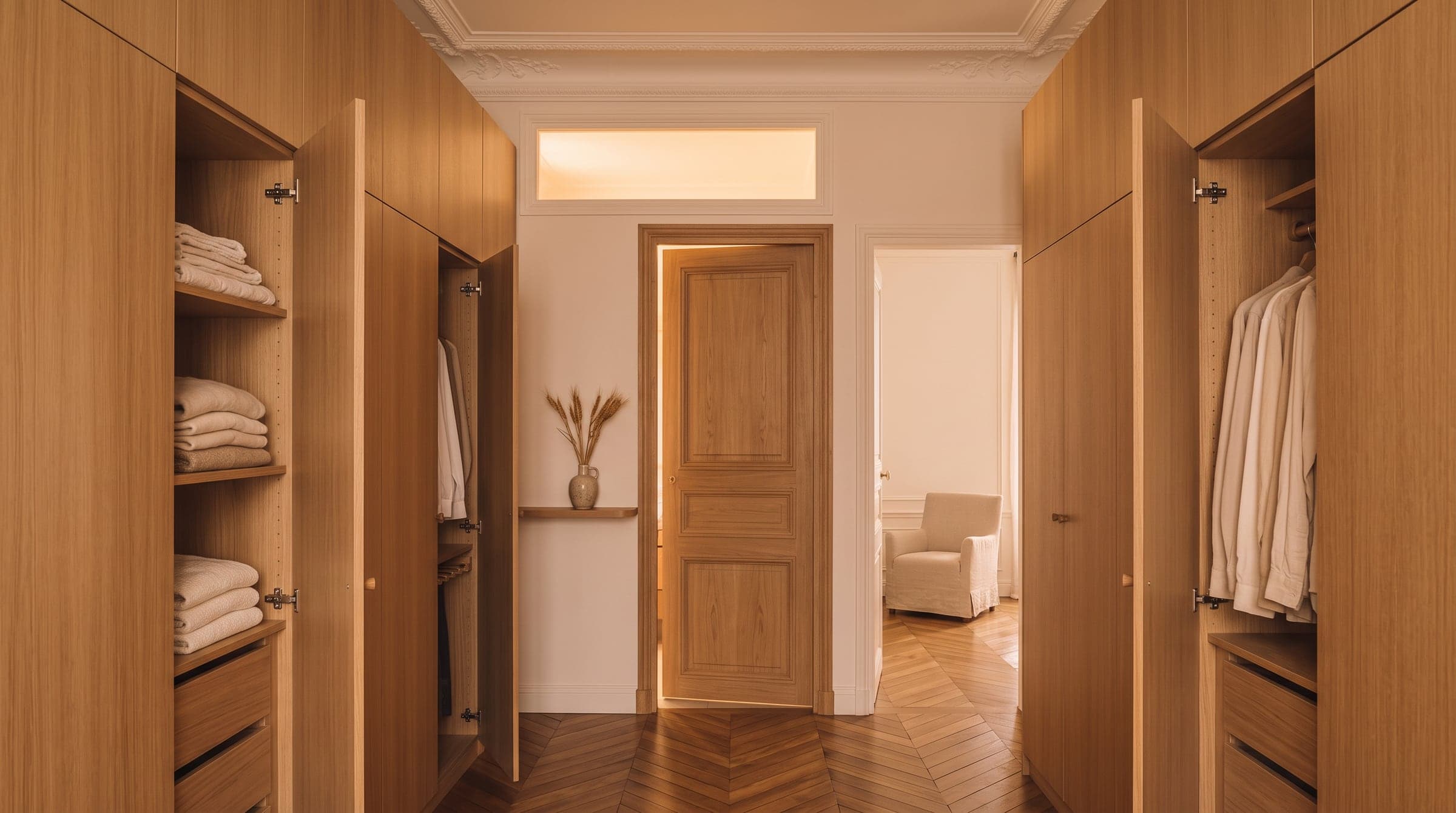Dressing tout en longueur avec penderies en chêne des deux côtés, porte ouverte sur une chambre et porte fermée au fond vers une salle d'eau