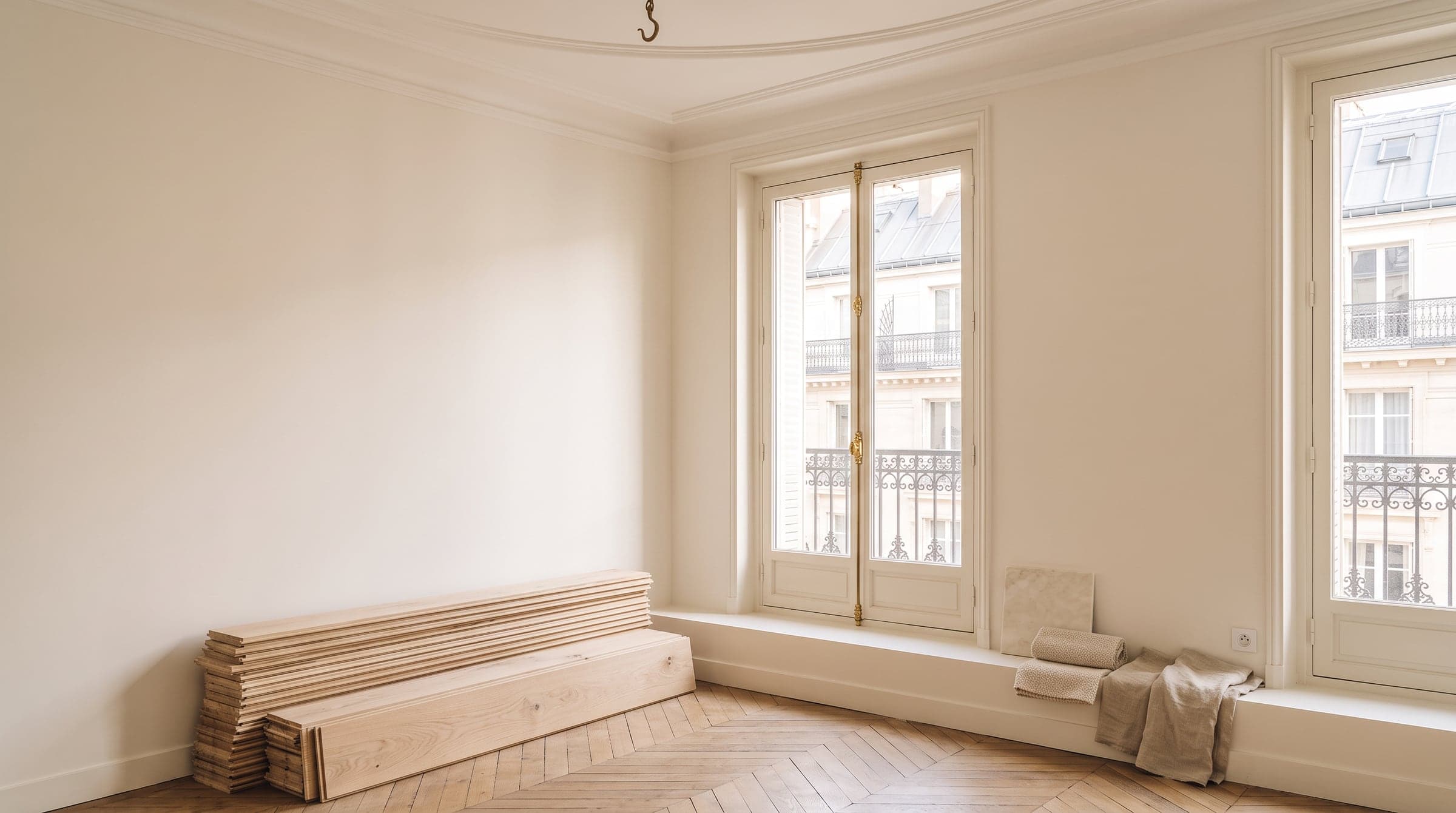 A Paris apartment room mid-renovation, oak flooring boards and marble samples arranged neatly on a windowsill in calm midday light