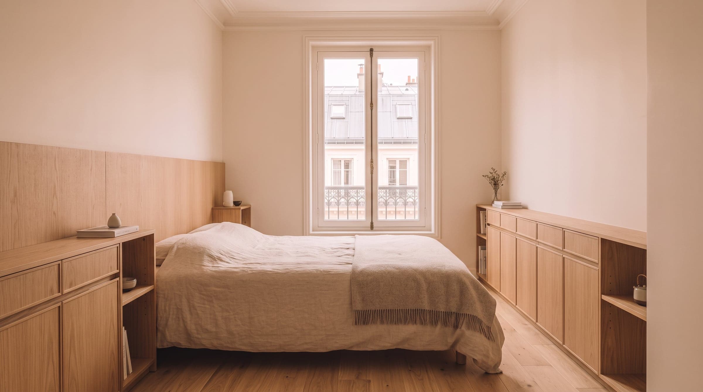 Bed framed by a headboard wall of low fitted storage in a small bedroom