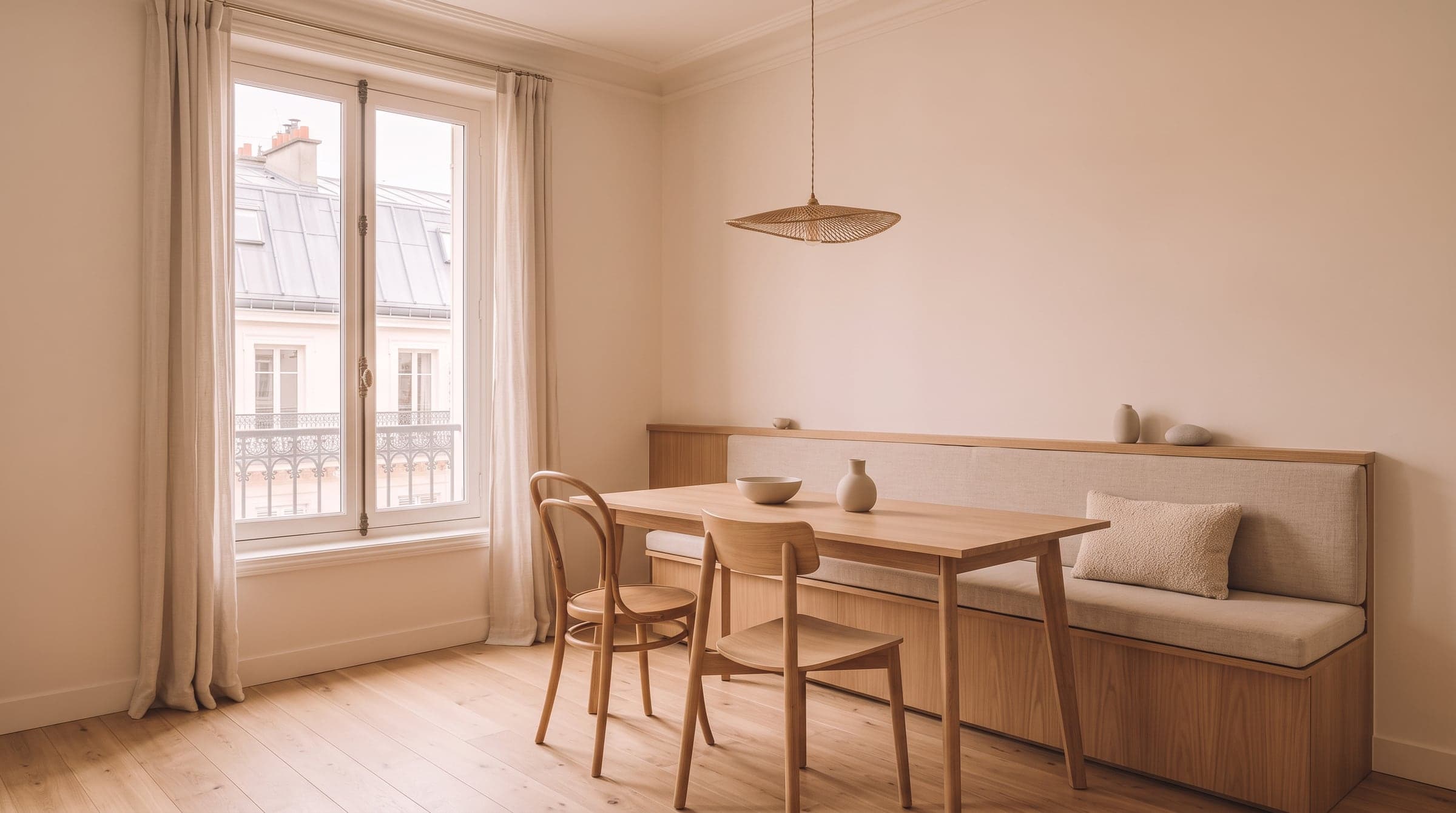 Built-in oatmeal linen bench along a wall in a small dining area, narrow oak table and two loose chairs