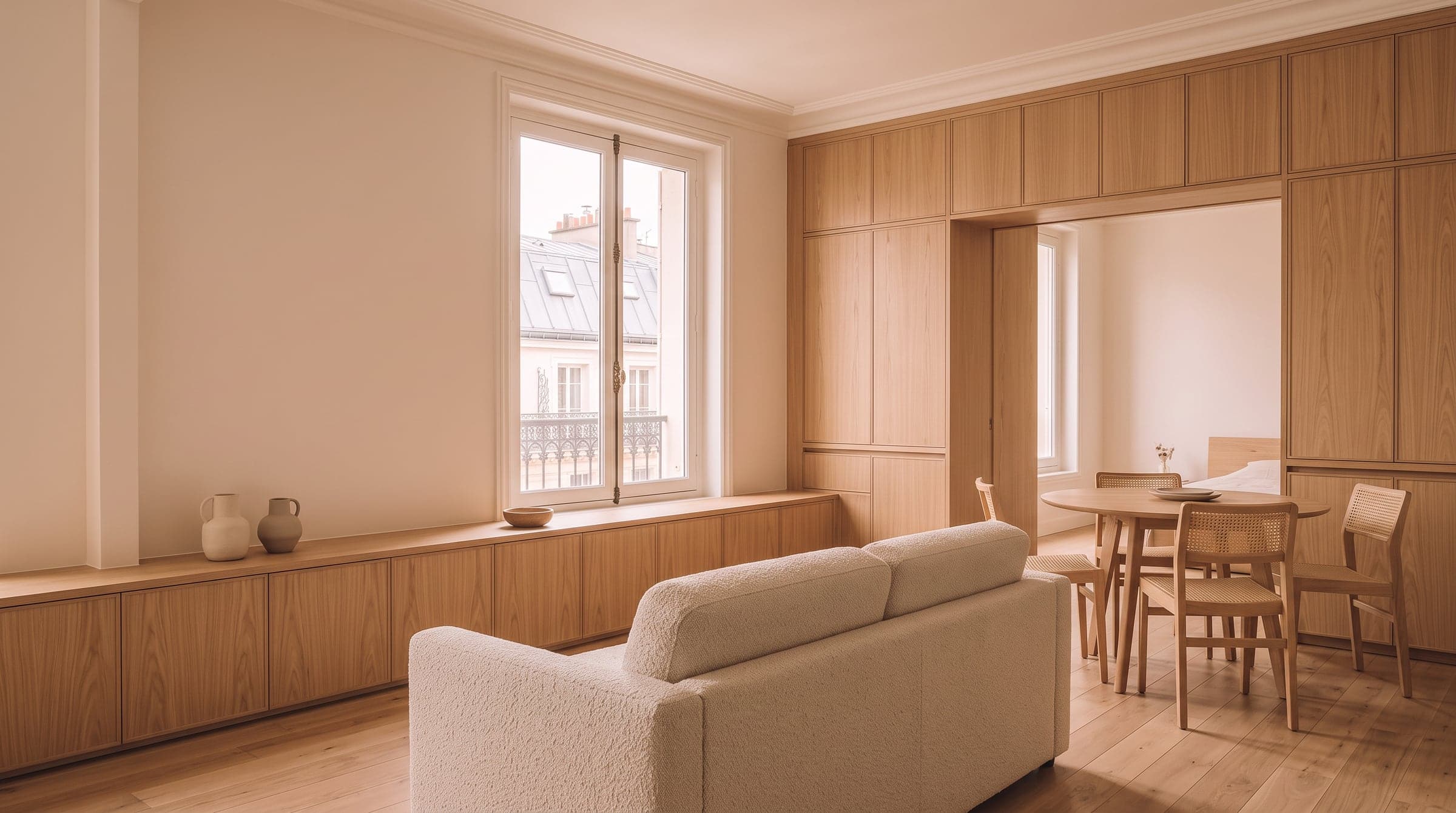 Low oak sideboard beneath a window in a tidy living-dining room, sofa facing away toward a round table